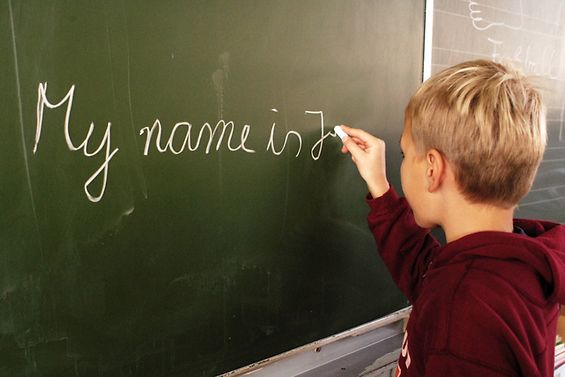 Ein Kind schreibt etwas auf englisch an die Tafel.