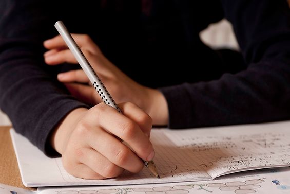 Eine Kinderhand schreibt mit Bleistift in ein Schulheft.