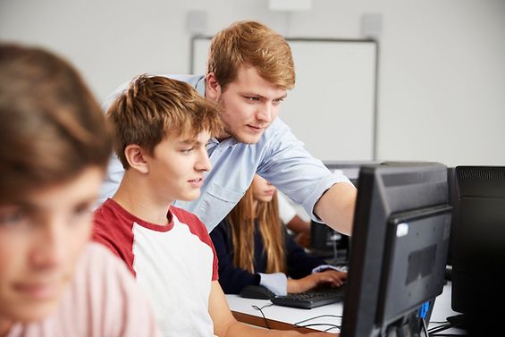 Schüler arbeiten am Computer und werden von einem Lehrer unterstützt.