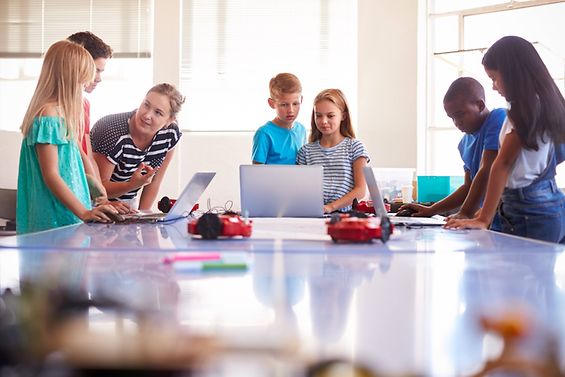 Eine Gruppe von jungen Schüler*innen besprechen an Laptops ein Thema mit ihrer Lehrerin.